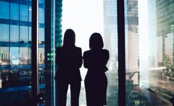 Back view of female colleagues in formal wear standing near window