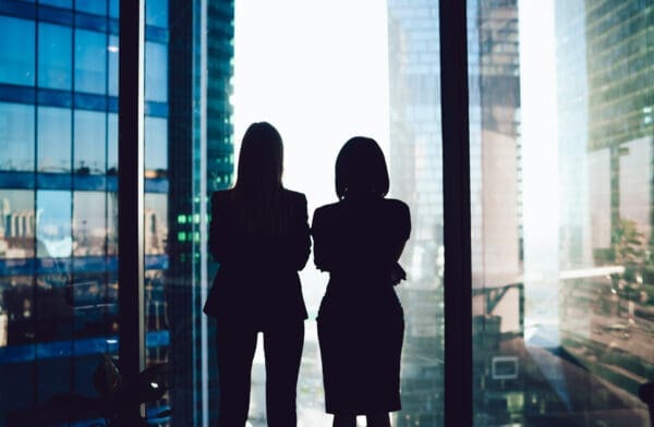 Back view of female colleagues in formal wear standing near window