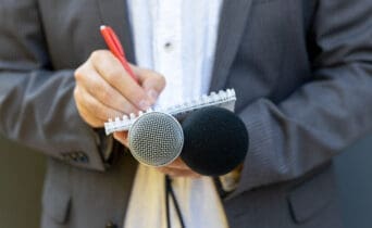 Correspondent or reporter at media event, holding microphone, writing notes. Journalism concept.