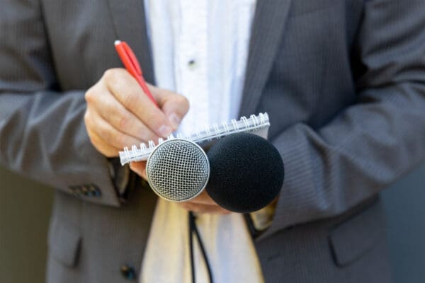 Correspondent or reporter at media event, holding microphone, writing notes. Journalism concept.